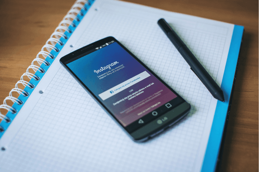 A phone with Instagram loaded on a notebook next to a pen