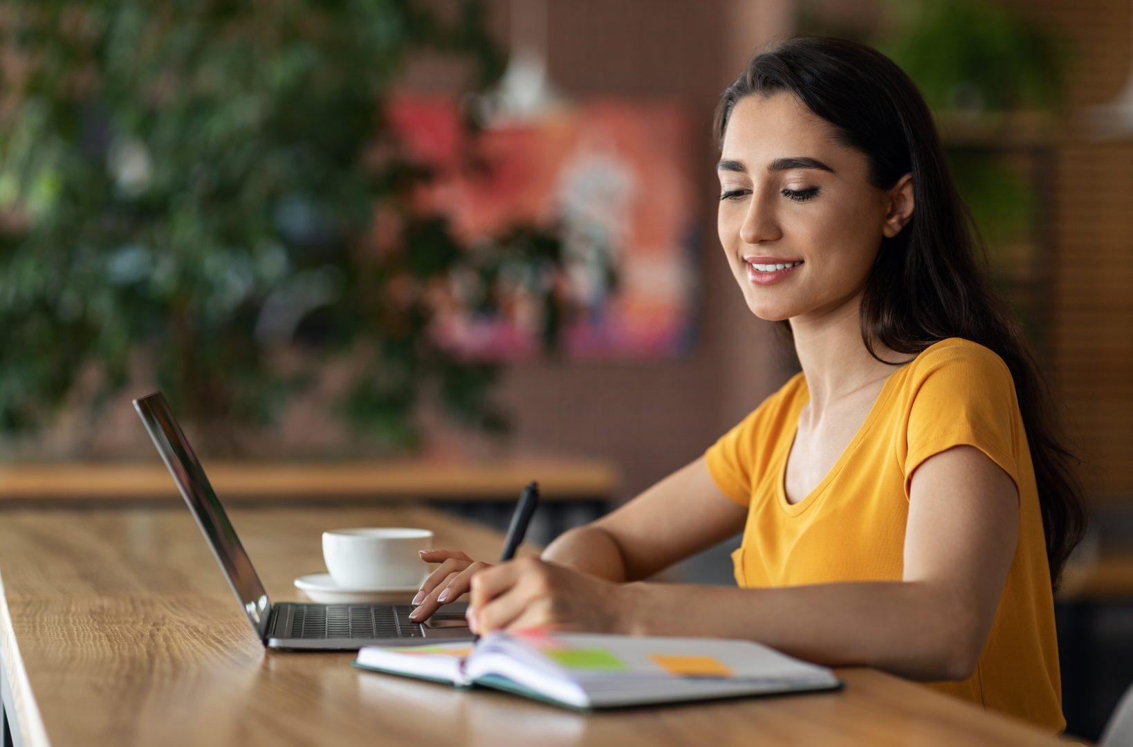 A woman on her laptop and writing in a notebook at the same time